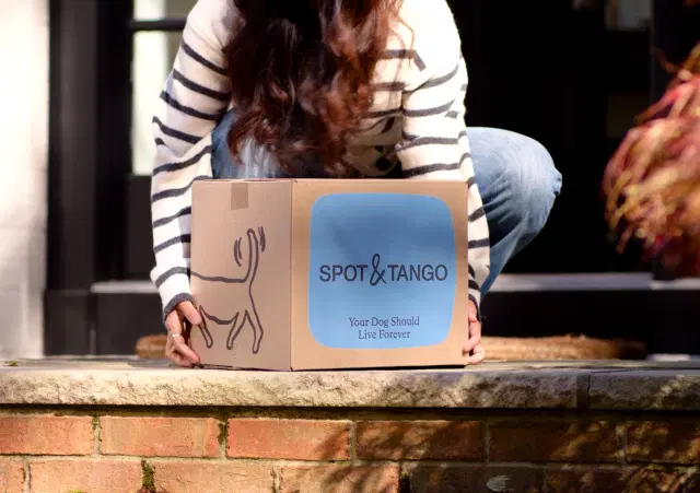 A woman picking up a box of Spot and Tango dog food from her doorstep